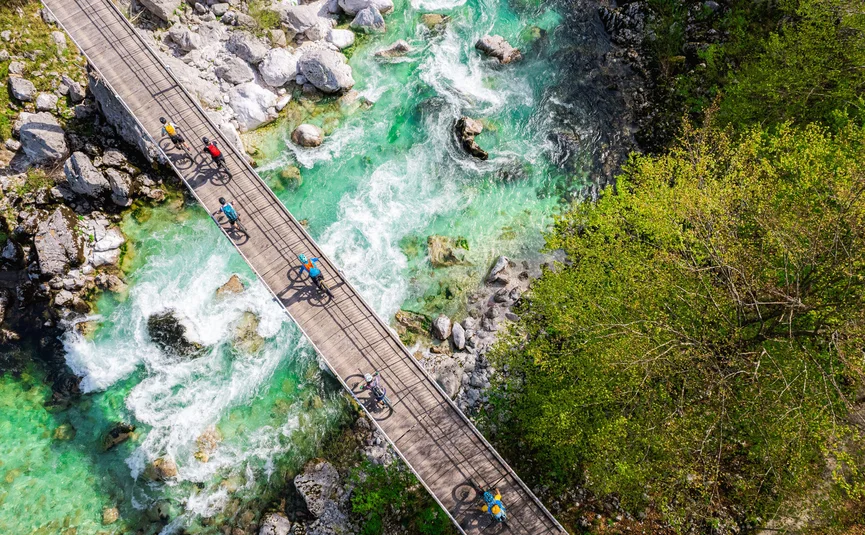 Mountainbike Urlaub in den Julischen Alpen © Soca Valley - Ziga Koren Radfahrer überqueren eine Brücke über einen klaren, grünen Fluss