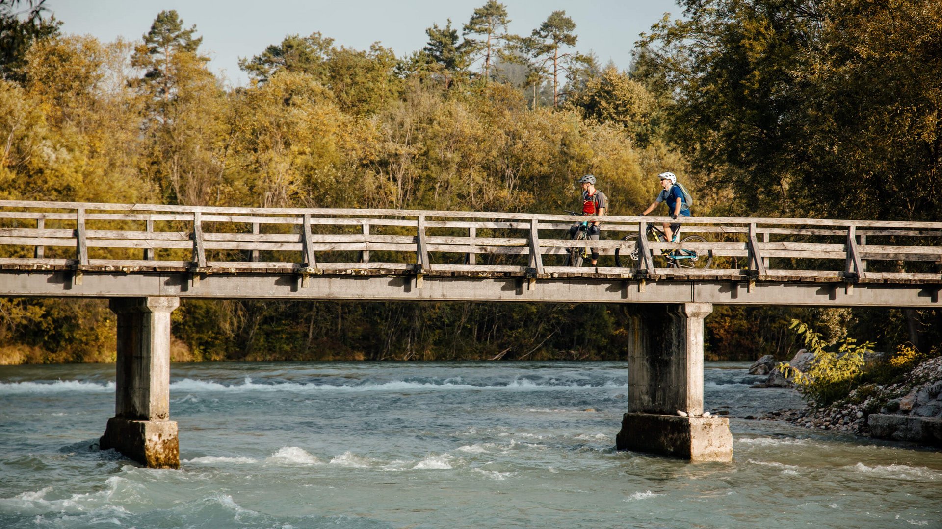 Zwei Radfahrer auf einer Holzbrücke über einem Fluss im Wald