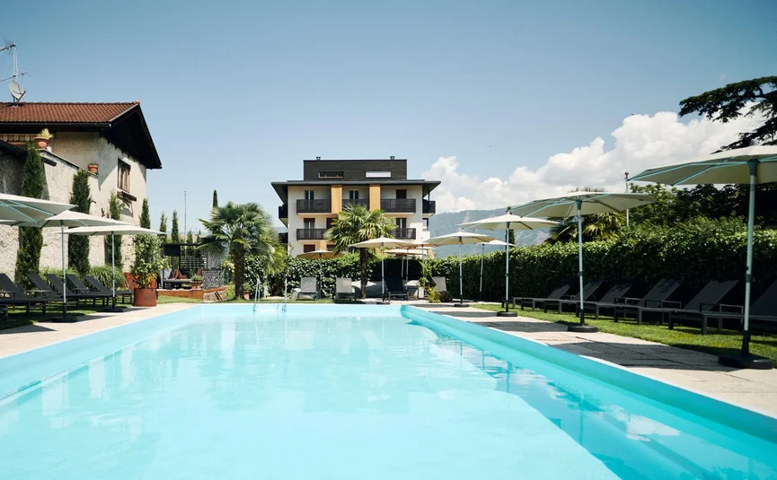 Freier Außenpool mit Liegestühlen und Sonnenschirmen vor einem Hotelgebäude