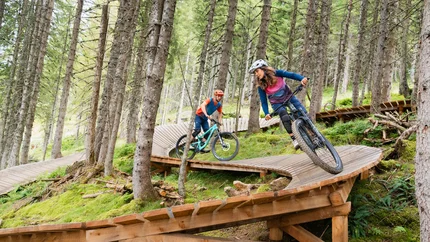Zwei Mountainbiker fahren auf einem holzverstärkten Trail im Wald