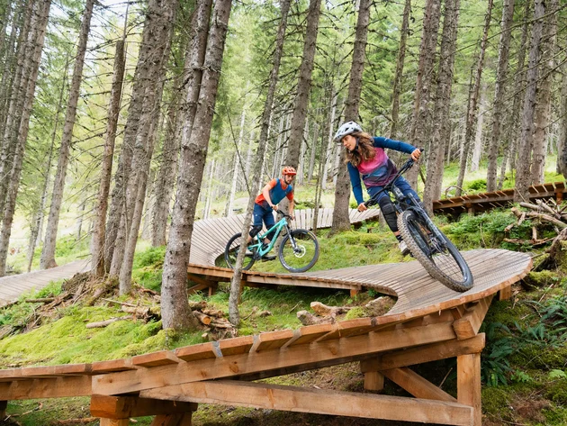 Unterwegs in Österreichs größter Bikeregion © Patrick Wasshuber Zwei Mountainbiker fahren auf einem holzverstärkten Trail im Wald