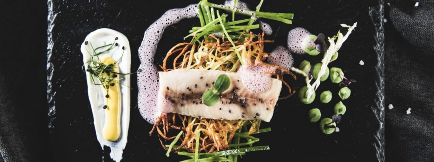Kunstvoll angerichteter Fisch mit Gemüse und Schaum auf schwarzem Teller