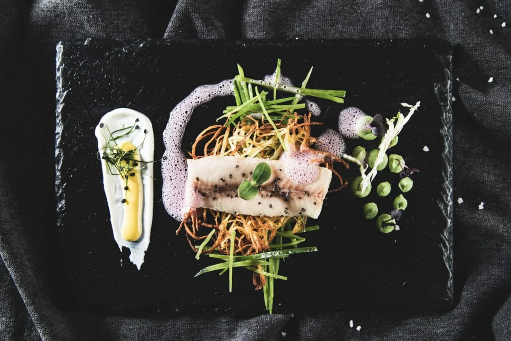 Kunstvoll angerichteter Fisch mit Gemüse und Schaum auf schwarzem Teller