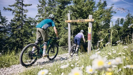 Twee personen mountainbiken op een bosweg genaamd Augst Trail