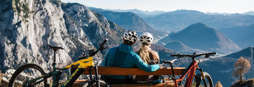 Zwei Radfahrer schauen von Bank auf Berglandschaft mit zwei Mountainbikes