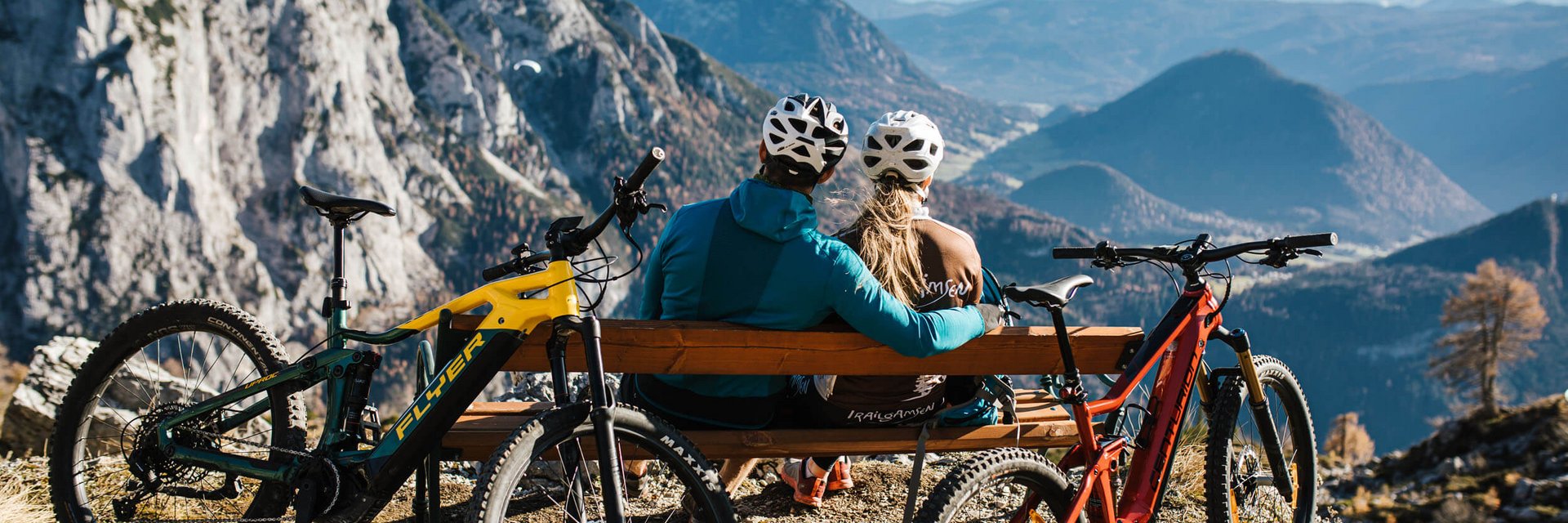 Twee fietsers op bank kijkend naar berglandschap met twee mountainbikes