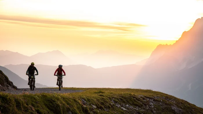 Zwei Radfahrer fahren bei Sonnenuntergang auf einem Bergweg