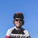 Fahrradfahrer auf felsigem Berggipfel mit Skulptur und Bergen im Hintergrund