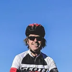 Fahrradfahrer auf felsigem Berggipfel mit Skulptur und Bergen im Hintergrund