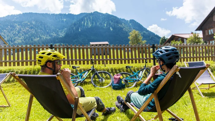 Twee fietsers rusten in ligstoelen op gras met uitzicht op bergen