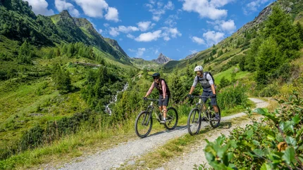 Zwei Mountainbiker auf einem Feldweg in grünen Bergen bei sonnigem Wetter