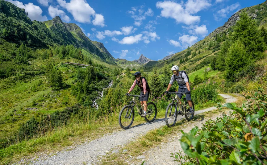 Two mountain bikers on a trail in green mountains on a sunny day