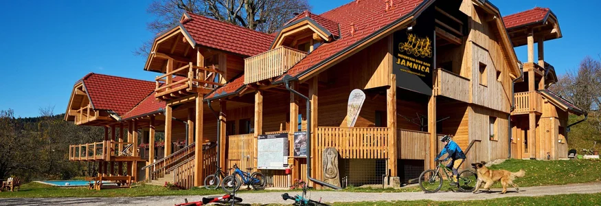 Holzhaus mit roten Dächern, Mountainbikes und Person mit Hund im Garten