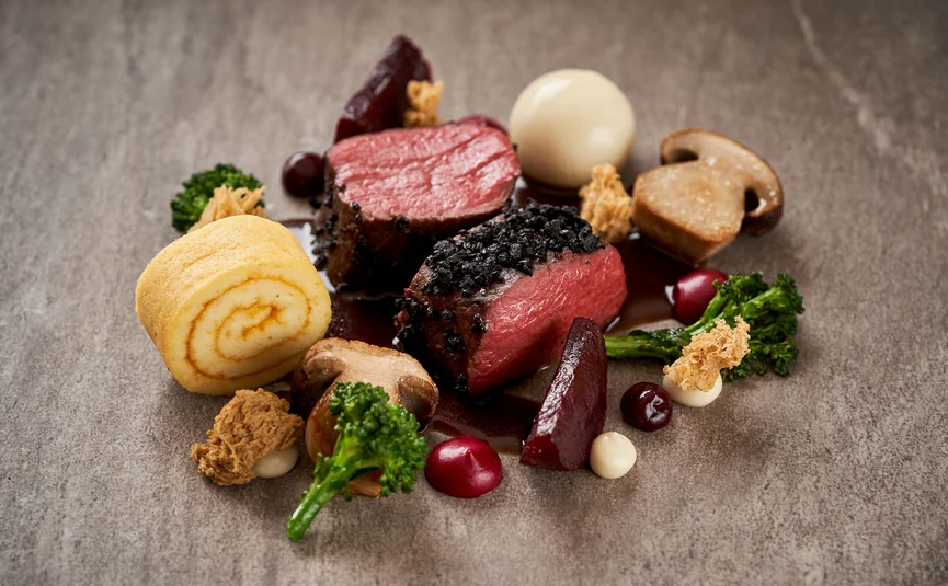 Gourmetgericht mit rosa gebratenem Fleisch, Pilzen und Gemüse auf grauem Teller