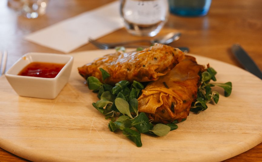 Two spring rolls with green salad and red dipping sauce on wooden board
