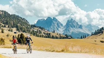 Zwei Radfahrer fahren auf einem Weg mit Berglandschaft im Hintergrund