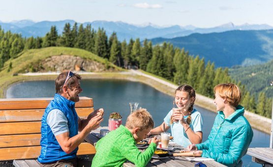 Familie isst zusammen draußen am See in den Bergen bei schönem Wetter