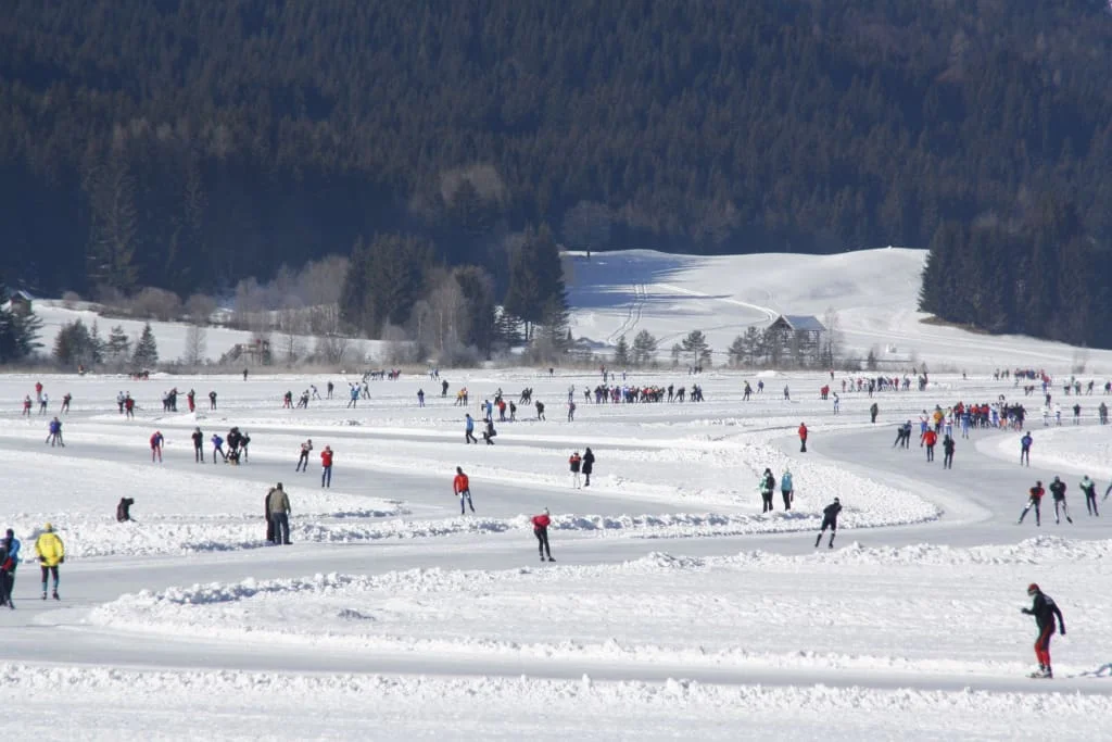 Viele Menschen beim Schlittschuhlaufen auf einer zugefrorenen Bahn im Winter