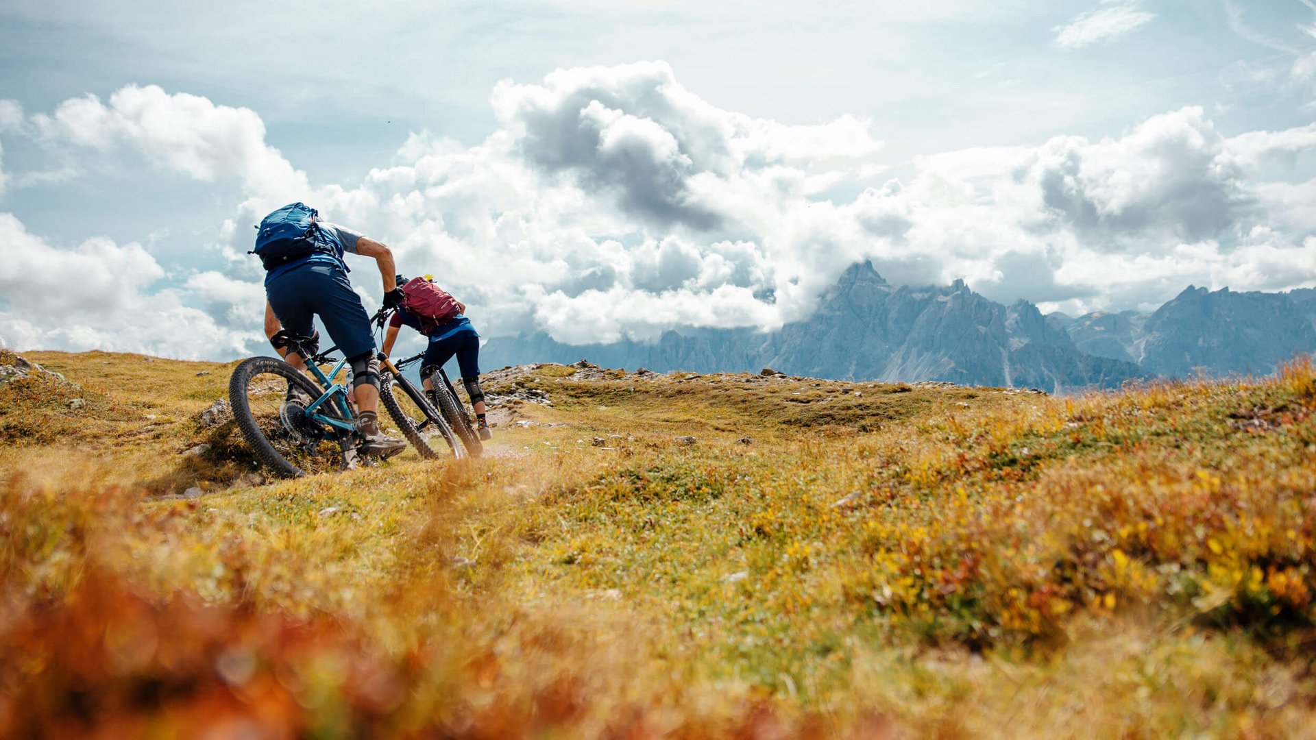 Zwei Mountainbiker fahren bergauf auf einem Pfad mit Bergen im Hintergrund
