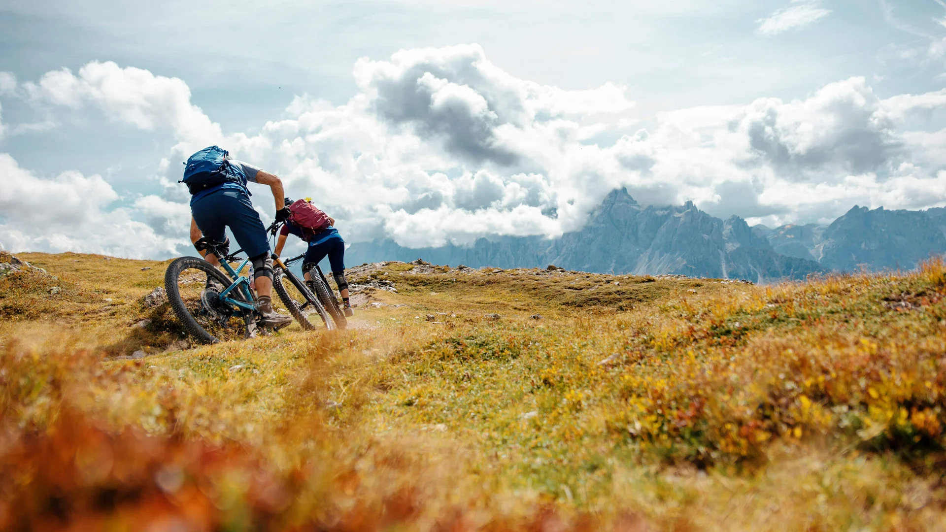 Spätsommer- & Herbstbiken in Toblach © David Karg Zwei Mountainbiker fahren bergauf auf einem Pfad mit Bergen im Hintergrund