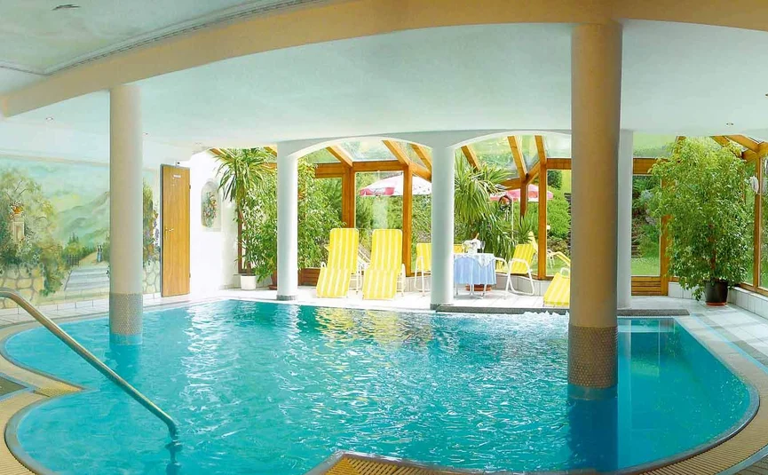 Hallenbad mit runden Säulen, Liegestühlen und Pflanzen in einem hellen Raum