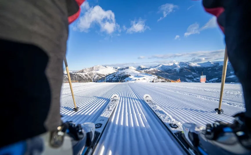 Ab auf die Piste im Jänner! Skifahrerblick auf frisch präparierte Piste und schneebedeckte Berge