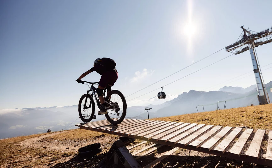 Mountainbiker fährt auf Holzbrücke in sonniger Berglandschaft