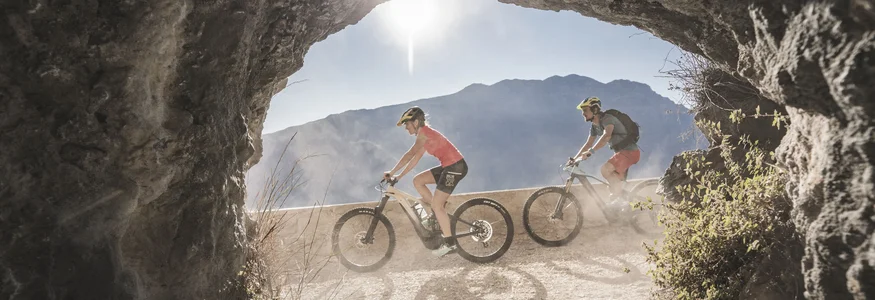 Two cyclists riding on a mountain trail seen through a rock opening