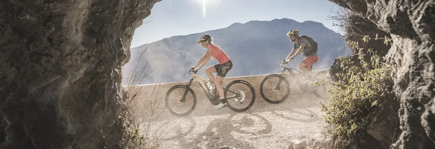 Zwei Radfahrer fahren auf einem bergigen Weg, gesehen durch eine Felsenöffnung