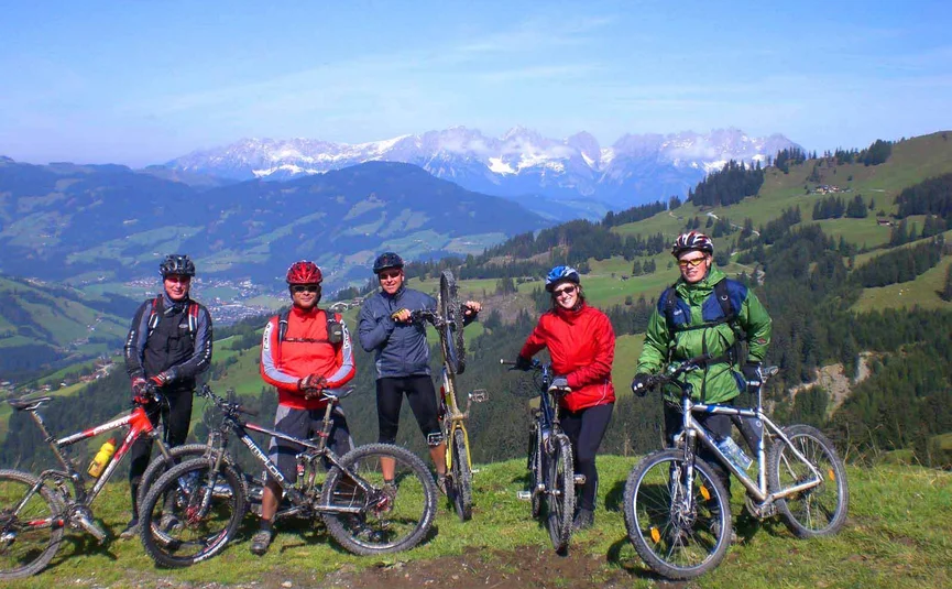 Fünf Mountainbiker mit Helmen vor Berglandschaft mit blassem Himmel
