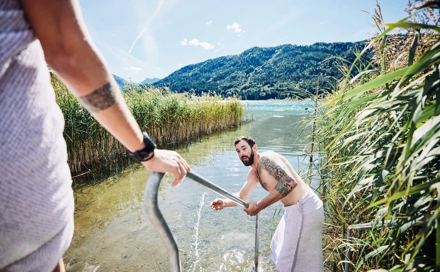 Mann in Handtuch steigt aus klarem Bergsee an Stange raus
