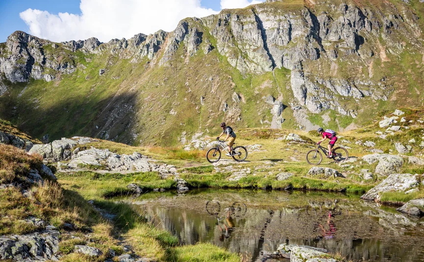 Twee mountainbikers fietsen langs een bergmeer in de Alpen