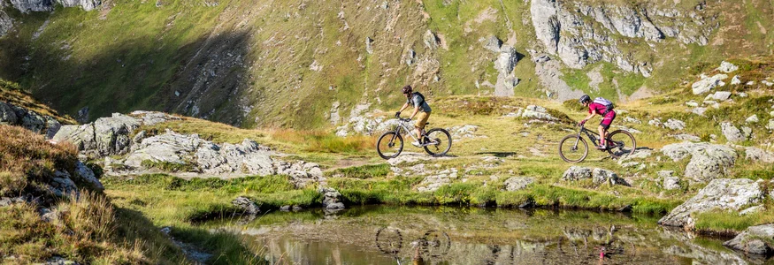Zwei Mountainbiker fahren an einem Bergsee in den Alpen vorbei