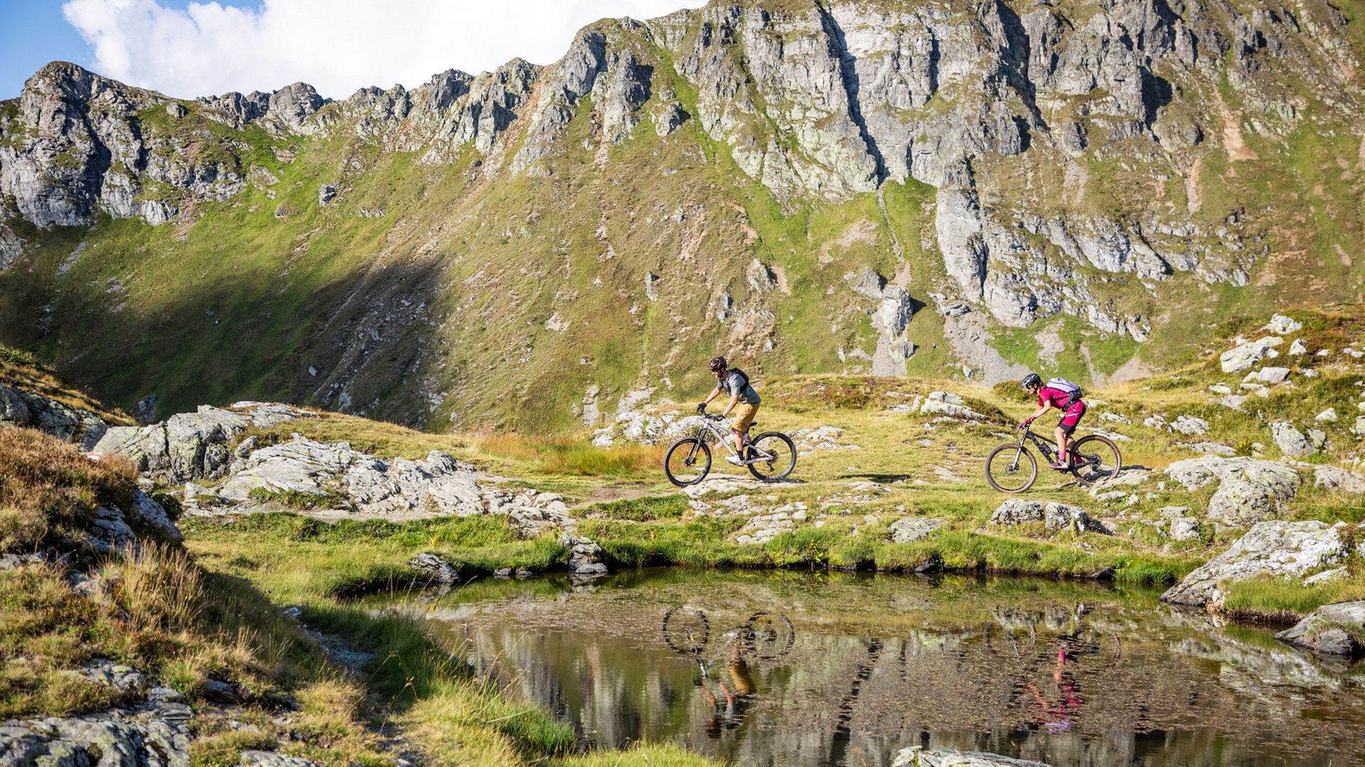 Zwei Mountainbiker fahren an einem Bergsee in den Alpen vorbei