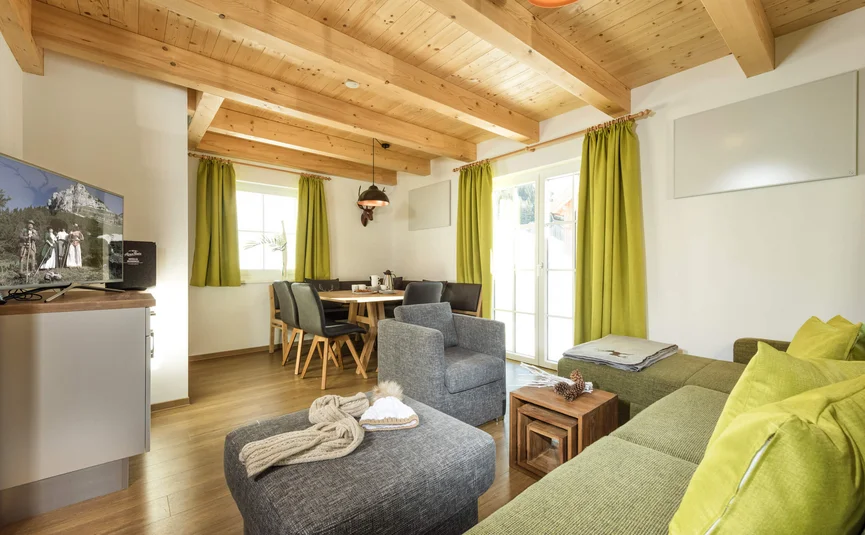 Gezellige woonkamer met houten balken, groene bank en eettafel.