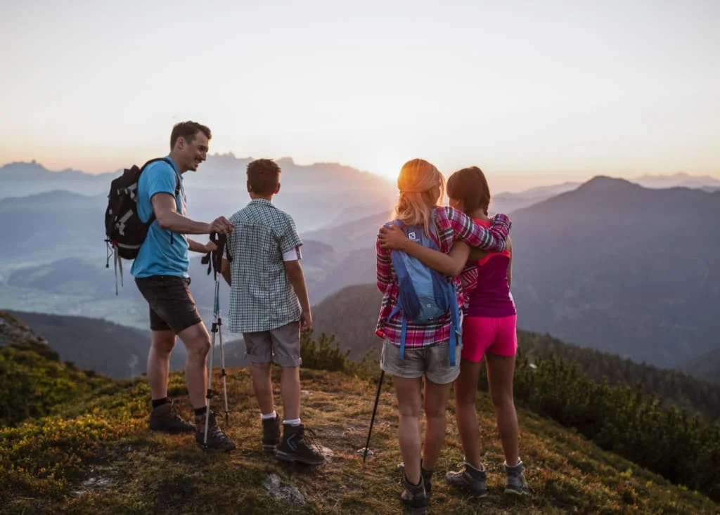 Vater und drei Kinder auf Berggipfel bei Sonnenuntergang beim Wandern
