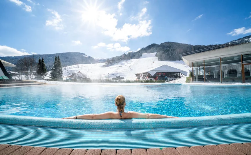 Vrouw ontspant in buitenzwembad met besneeuwde bergen en blauwe lucht