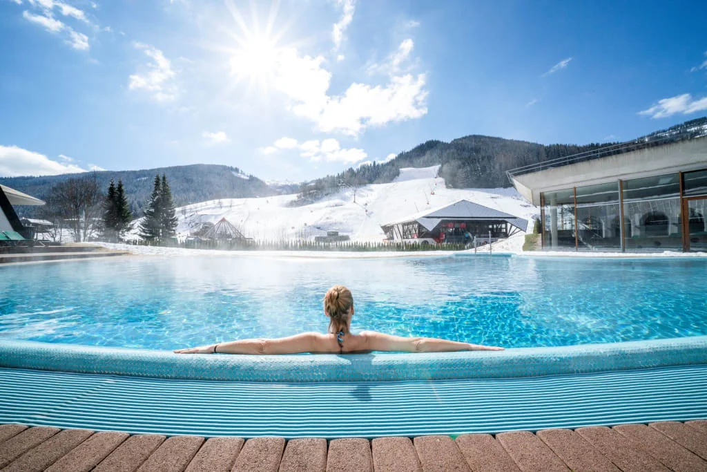 Sonnenskilauf & Therme / 3 Nächte Vrouw ontspant in buitenzwembad met besneeuwde bergen en blauwe lucht