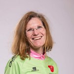 Lächelnde Frau in Mountainbike-Trikot und Jeans vor hellem Hintergrund