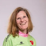 Lächelnde Frau in Mountainbike-Trikot und Jeans vor hellem Hintergrund