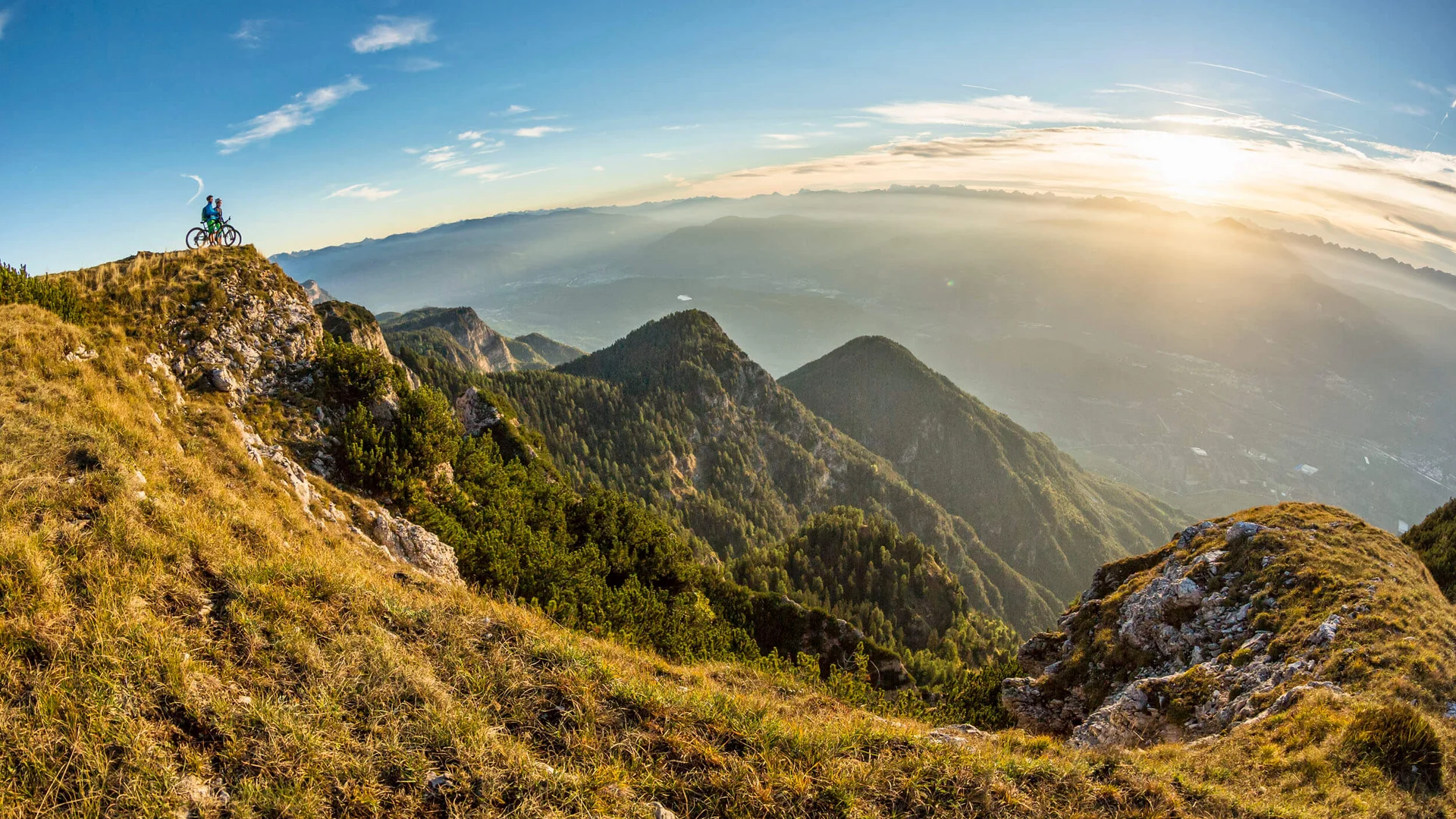 Zwei Radfahrer auf Berggipfel mit Sonnenuntergang und Panorama