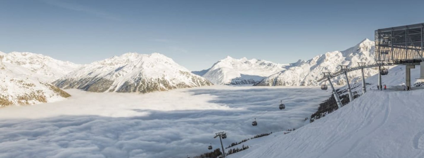 Schneebedeckte Alpen mit Skilift und Wolkenmeer im Tal