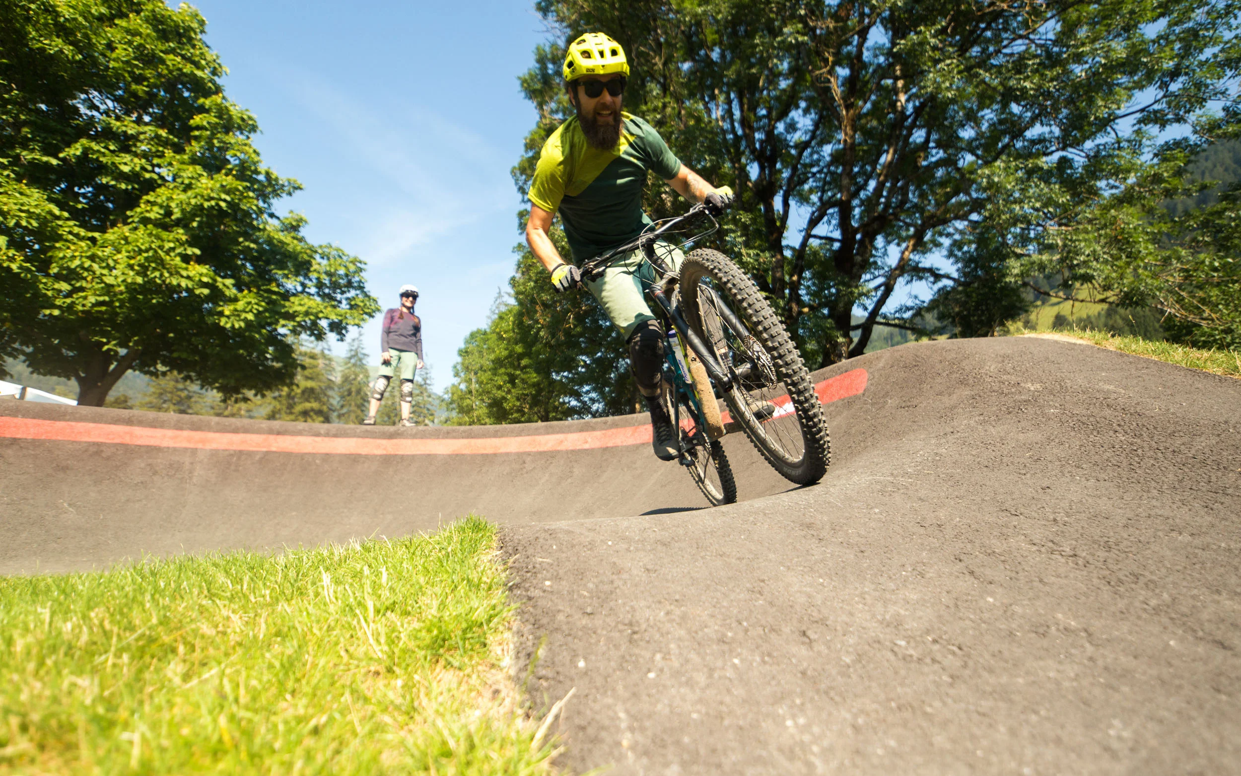 Mann fährt Mountainbike auf Pumptrack bei sonnigem Wetter