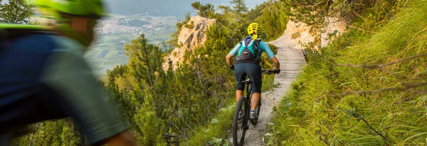 Zwei Mountainbiker auf einem schmalen Gebirgspfad mit grünem Bewuchs