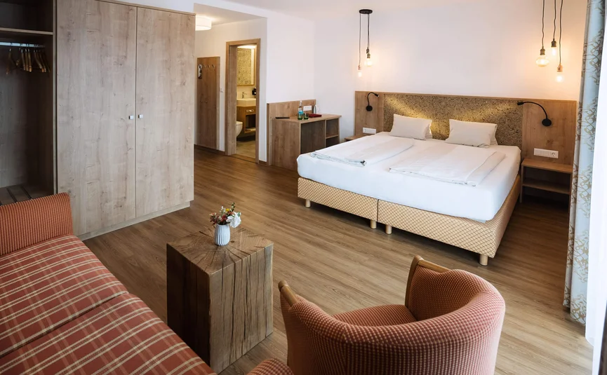 Modernes Hotelzimmer mit Doppelbett, Holzmöbeln und Sitzbereich mit Sesseln