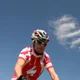 Radfahrer fährt auf Mountainbike vor Holzhäusern auf Grasland