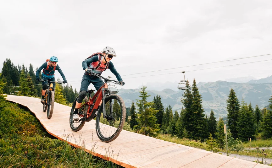 Zwei Mountainbiker fahren auf einem Holzweg durch den Wald in den Bergen