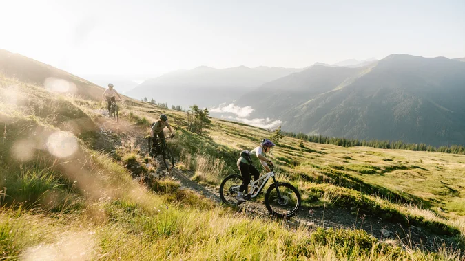 Drei Mountainbiker fahren auf einem Bergpfad im Sonnenlicht