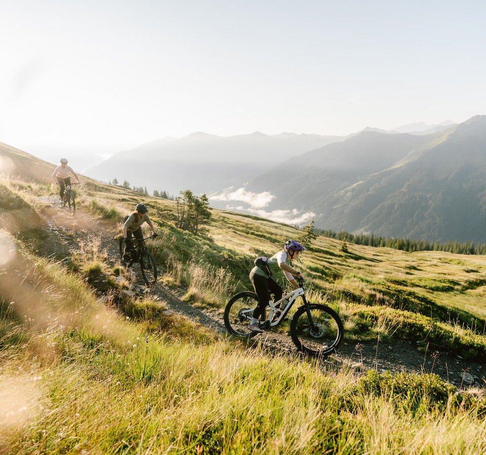 Drei Mountainbiker fahren auf einem Bergpfad im Sonnenlicht