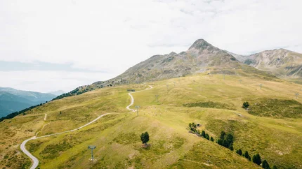 Grüne Berglandschaft mit Wanderwegen und Sesselliften bei bewölktem Himmel